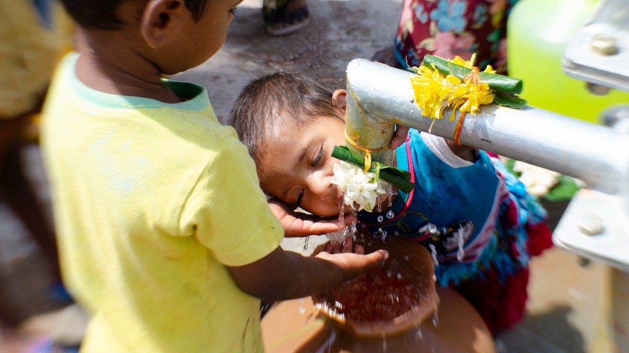 Dos niños bebiendo agua en una fuente de agua potable